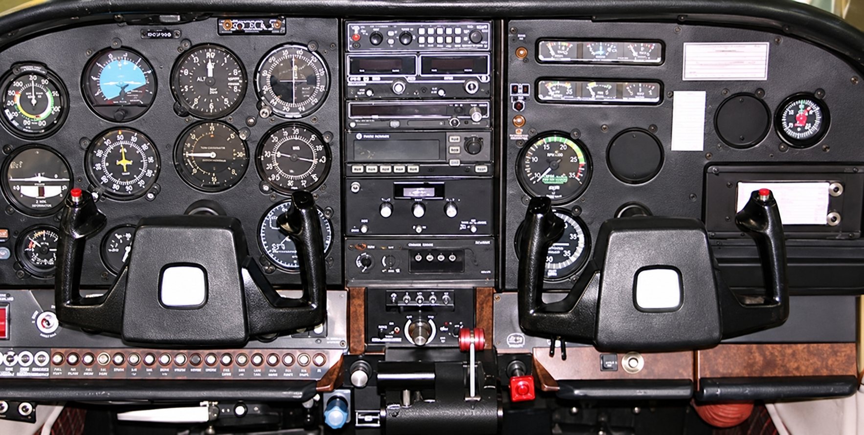 Vue du tableau de bord d’un petit avion avec ses instruments de vol, sa radio centrale et deux manches de pilotage.