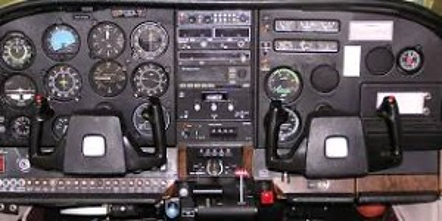 Vue du poste de pilotage d’un petit avion avec ses instruments de vol, sa radio et ses deux manches.